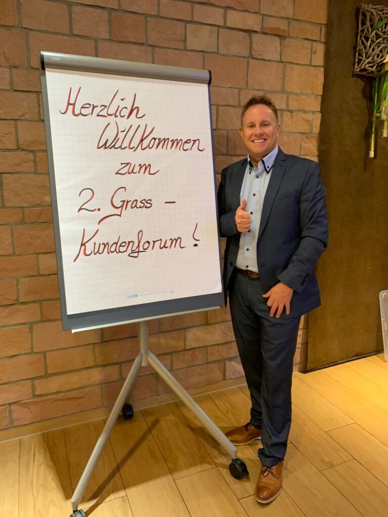 Heiko Friedrich am Board mit der Aufschrift "Herzlich Willkommen zum 2. GRASS-Kundenforum